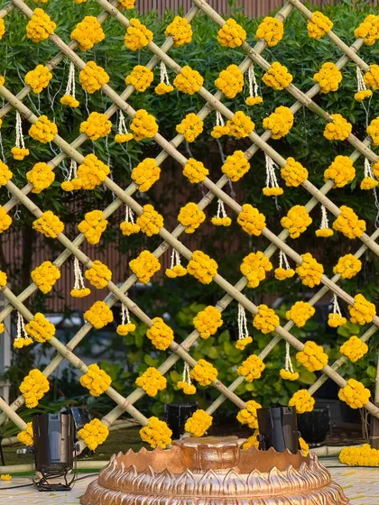 A detailed shot of the marigold and tuberose tassel backdrop. The intricate weaving of flowers on the bamboo grid creates a beautiful texture and a classic look for a Haldi ceremony.
