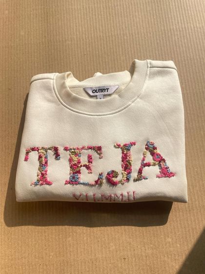 This custom sweatshirt features the name 'TEJA' embroidered with a dense floral pattern, with a special date stitched below. A beautiful anniversary or birthday gift.