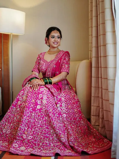 A full-length portrait of the bride seated, showcasing the magnificent volume and embroidery of her pink lehenga. She looks every bit the modern-day princess.