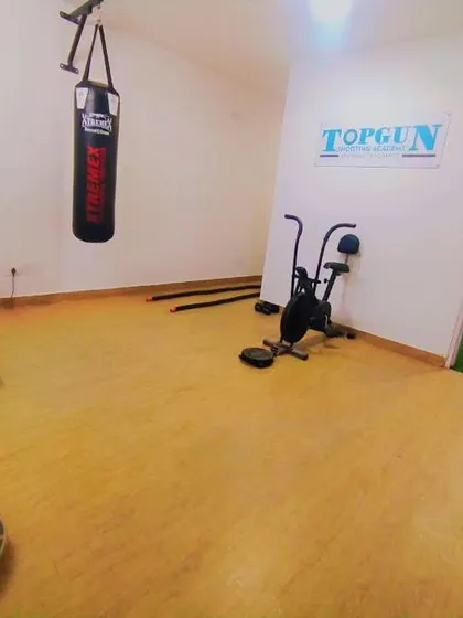 This is our dedicated fitness area, equipped specifically for shooters. You can see the treadmill for endurance, a punching bag for power, an exercise bike for cardio, and a balance board in the foreground, a key tool we use for stability training.