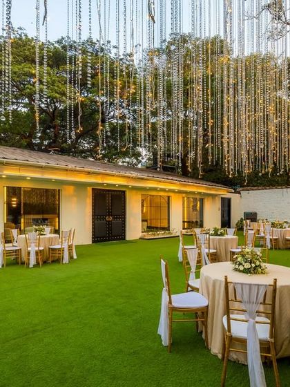 The beautiful lawn area outside the banquet hall, set up for an evening event. The hanging fairy lights create a magical, dreamlike ambiance, extending the elegance of the interior to the outdoor space.