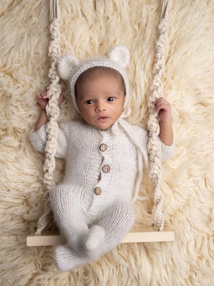 This little bear is awake on the swing, looking around with wide-eyed wonder.