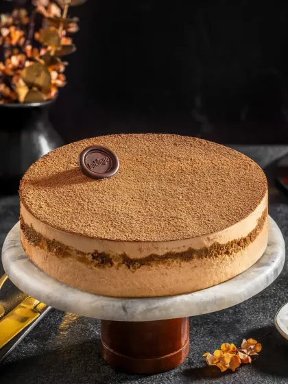 A tiramisu cake with a dusting of cocoa, styled with coffee beans and a cup of black coffee to suggest its flavor profile.