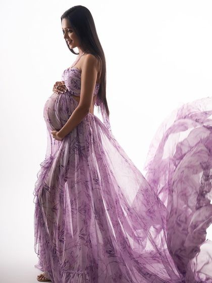 This high-key portrait showcases a beautiful floral lavender gown with a flowing train. The bright, clean background emphasizes the delicate pattern and graceful movement of the fabric.