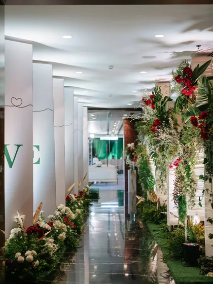 A beautifully designed walkway leading to the main event space. The path is lined with white and red flowers, and one side features panels telling the couple's love story, creating a personal and meaningful journey for the guests.