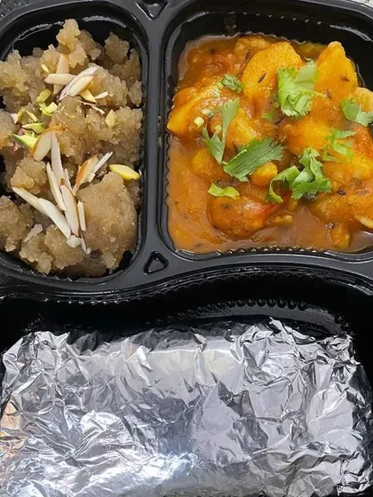 A special tiffin combo featuring a savory potato curry and a portion of sweet suji halwa. The rotis are packed in foil to ensure they arrive fresh and warm.