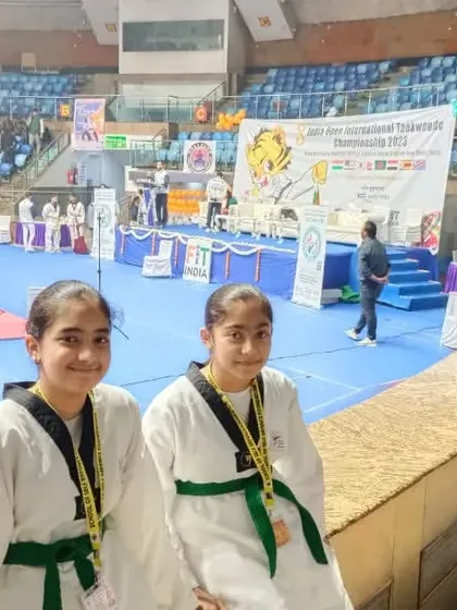 Two of our students, dressed in their taekwondo uniforms with green belts, pose for a photo at the international championship venue. Their smiles reflect their pride and excitement.