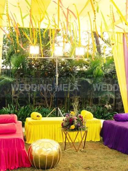 A classic and colorful outdoor mehandi setup. The bright yellow and purple seating with matching drapes creates a cheerful and inviting space for guests to relax and celebrate.