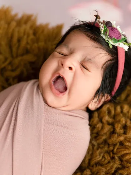 A candid close-up of a newborn baby yawning, captured while swaddled in a soft pink wrap. I always look for these unposed, fleeting moments that show your baby's true character.