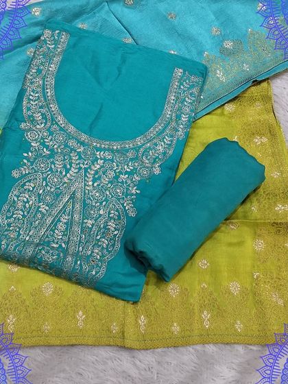 This unstitched dress material features a teal top with heavy silver embroidery around the neck, paired with a shaded green and yellow dupatta.