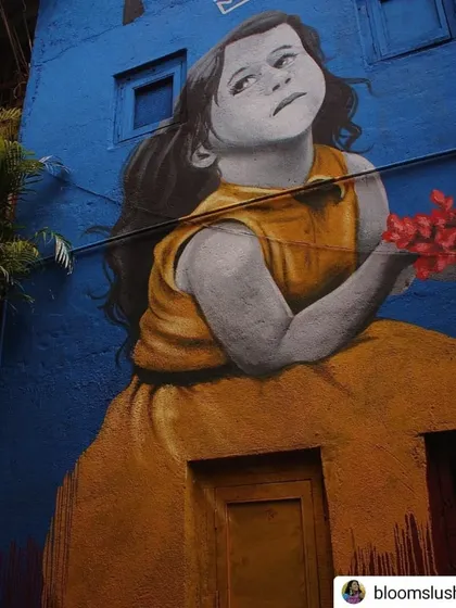 A beautiful and poignant mural of a young girl in a yellow dress, looking up at the sky. The piece, part of the 'Chal Rang De' project, brings a touch of innocence and hope to the urban environment.