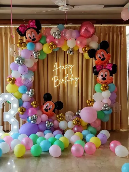 A colorful Mickey and Minnie Mouse theme for a 3rd birthday. This home setup includes a balloon arch with character foil balloons and a marquee number '3'.