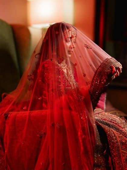 A dramatic bridal portrait with a red veil. The lighting creates a moody and romantic feel, highlighting the richness of her attire.