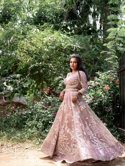 A full-length shot of a model in a pink lehenga, posing gracefully in a garden.