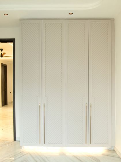 A beautiful example of a custom wardrobe with a chevron-patterned texture and elegant long handles. The built-in lighting at the base adds a floating effect.