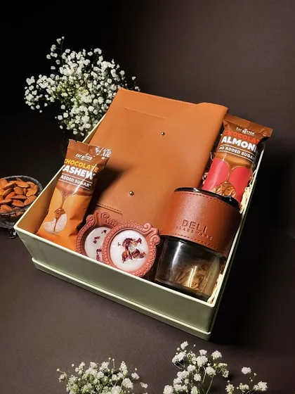A sophisticated Diwali gift box containing a leather-finish journal, a matching tumbler, and healthy snack bars, perfect for a corporate client or colleague.
