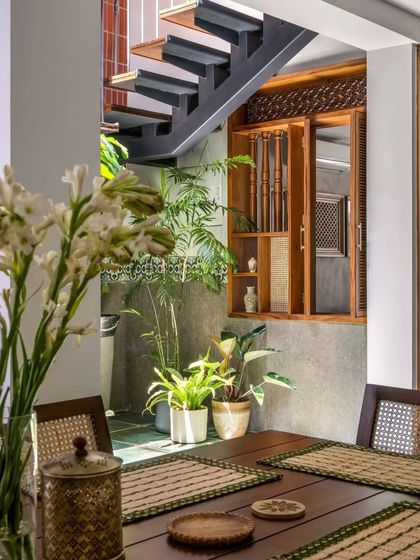 A view from the dining table towards the courtyard staircase, where light from above illuminates the indoor plants and traditional window.