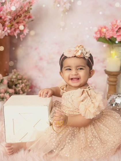 A smiling baby girl plays with a white block in a dreamy, all-pink floral studio setup.