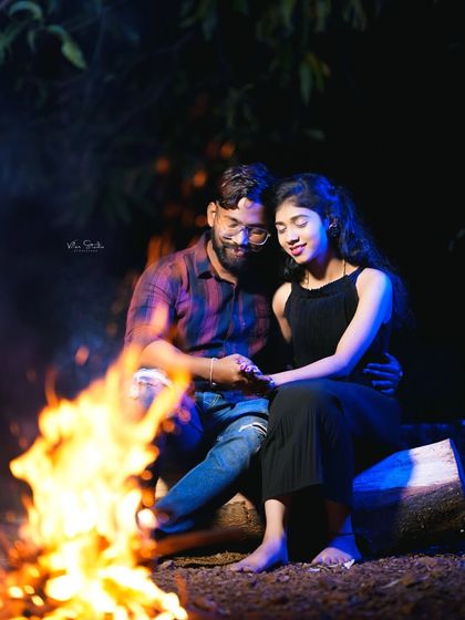 A quiet, intimate moment by the fire. The couple holds hands, lost in their own world, creating a deeply romantic and peaceful photograph.