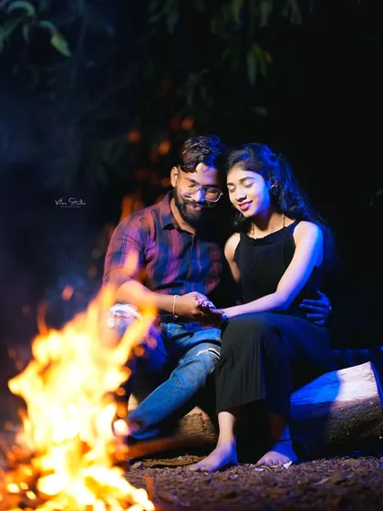 A quiet, intimate moment by the fire. The couple holds hands, lost in their own world, creating a deeply romantic and peaceful photograph.