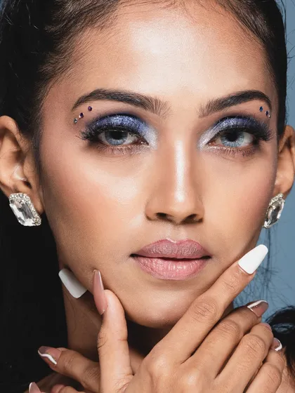 A captivating beauty headshot with a direct gaze. The small rhinestones near the eye add a creative touch to the glamorous makeup.
