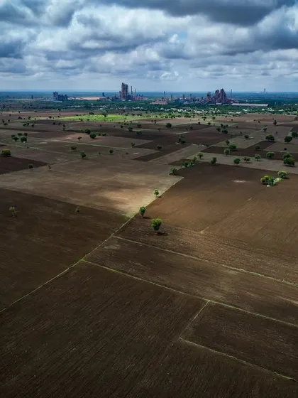 Vast agricultural fields in Karnataka, with an industrial plant in the far distance. A commentary on the changing landscape of rural India.