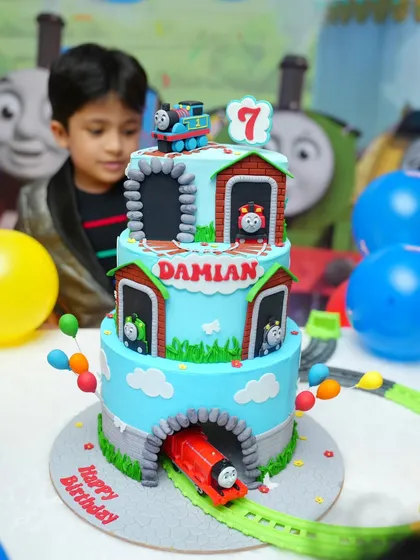 Damian admiring his three-tier Thomas cake, complete with tunnels and all his favorite characters peeking out.