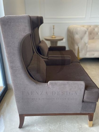 A pair of elegant, high-back lounge chairs in a deep brown fabric. Paired with a sleek, modern side table, they create a sophisticated and comfortable seating area by the window.