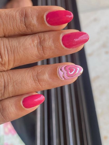 A simple and sweet design with a solid pink manicure and a single accent nail with a layered heart design.