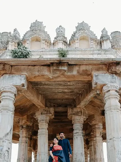 A low-angle, wide shot that emphasizes the magnificent, ancient architecture of the Melkote temple. The couple, though small in the frame, is the central focus of this epic scene.