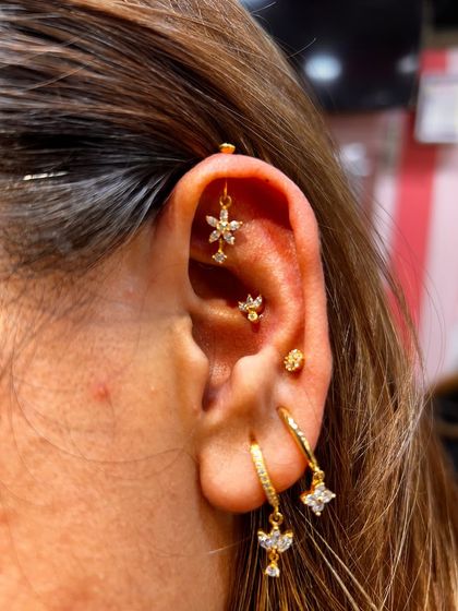 A beautiful example of a curated ear in gold tones. This stack features a floral hanging in the helix, a tragus stud, and multiple hoops and studs for a layered, warm look.