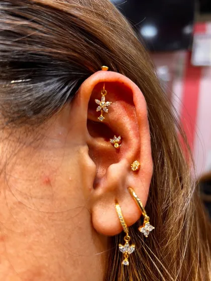 A warm, gold-toned ear stack featuring a floral hanging, a tragus stud, and sparkling hoops for a cohesive and sunny look.