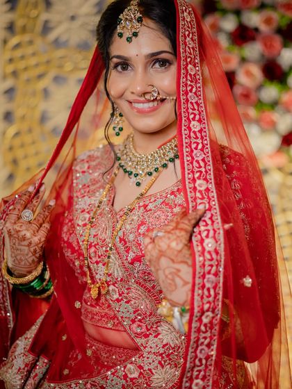 A beautiful portrait of the bride revealing her full reception look. The red lehenga, emerald green jewelry, and flawless makeup come together to create a truly regal appearance.