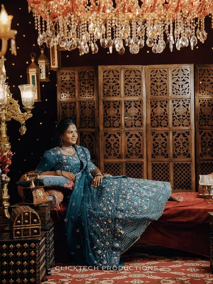 A solo portrait of the bride-to-be, seated like royalty in a lavishly decorated room. This shot focuses on her beautiful blue lehenga and confident pose.