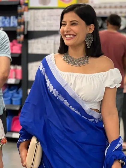 A happy, candid moment. The off-shoulder blouse and modern clutch give this traditional saree look a fresh, youthful feel.