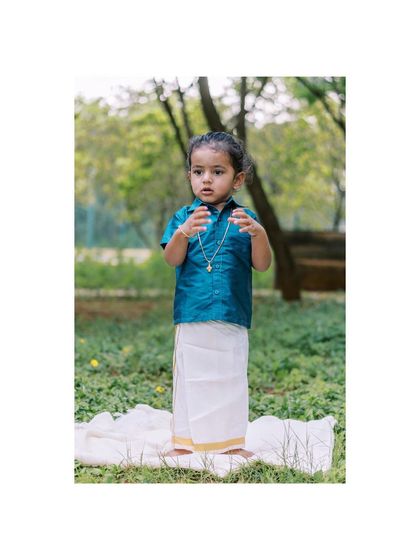 A full-length shot of a little boy in traditional ethnic wear. The vibrant colors look stunning against the green backdrop.