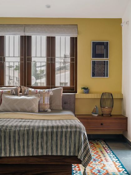 This bedroom in Relic House is a cozy retreat, with a warm yellow feature wall that radiates positivity. We layered textures with a striped bedcover, a colorful dhurrie rug, and patterned cushions, while the floating wooden nightstand maintains a clean, uncluttered feel.