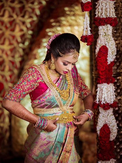 A stunning shot of Sushmitha getting ready for her Muhurtham. The focus is on her beautiful multi-hued Kanjivaram saree, with makeup tones chosen to complement the pink and green.