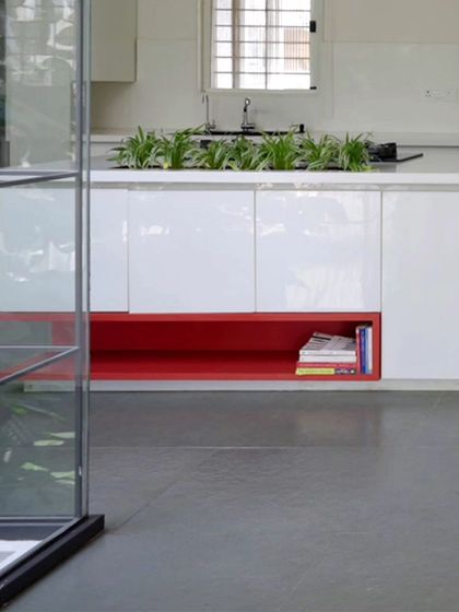 Even the kitchen has a touch of playful color. A bright red open niche in the otherwise clean, white cabinetry provides a perfect spot for cookbooks and adds a dash of personality to the functional space.