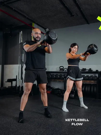 A coach and client perform kettlebell swings in unison. This powerful exercise is fundamental to our kettlebell flow sessions, building explosive power and cardiovascular fitness.