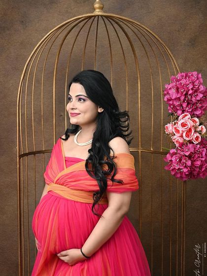 A vibrant and joyful portrait. The bright pink and orange gown pops against the warm brown background and golden birdcage prop.