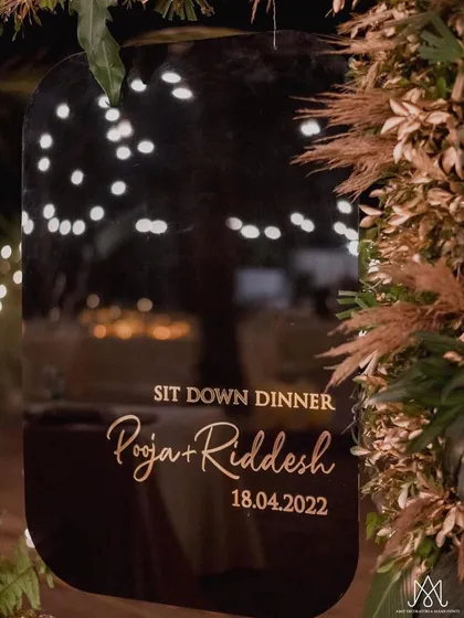 A personalized welcome sign for a sit-down dinner, elegantly scripted on a dark, reflective surface and framed by pampas grass.