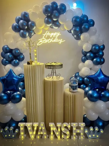 A classic blue and white balloon arch for a boy's birthday party. The setup includes star-shaped foil balloons, a neon sign, and light-up letters.