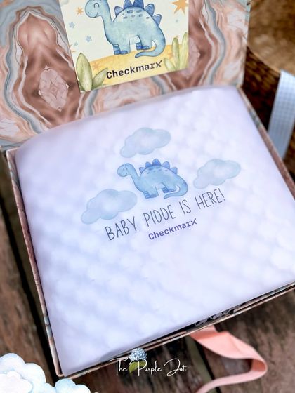 The unboxing experience is part of the gift. Here, personalized tissue paper with a dinosaur motif announces "Baby Pidde is Here," creating a special moment of discovery.