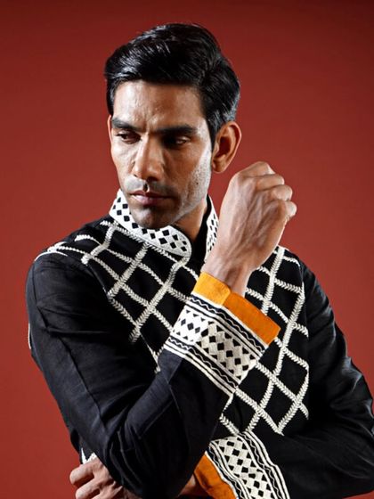 A black raw silk Jawahar jacket with a bold, white geometric pattern. The pop of mustard yellow on the kurta cuff adds a striking and unexpected detail.