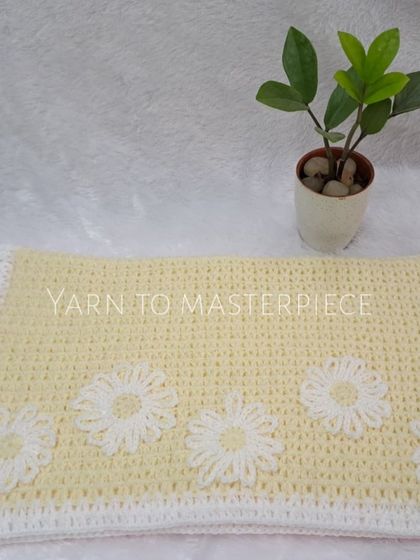 The yellow and white baby blanket laid out. The soft yellow is a lovely gender-neutral option, and the white flowers add a touch of sweetness.
