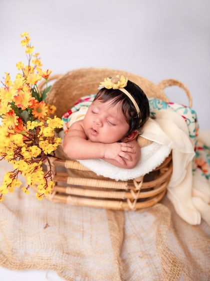 A newborn baby rests her head on her hands in a basket filled with yellow flowers. The warm, earthy tones are so beautiful and calming.