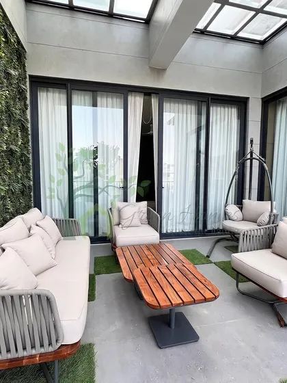 A photograph of a finished balcony project in Yojna Vihar. This enclosed space features a glass skylight, a vertical green wall, and comfortable woven furniture, turning a small balcony into a cozy, private retreat.