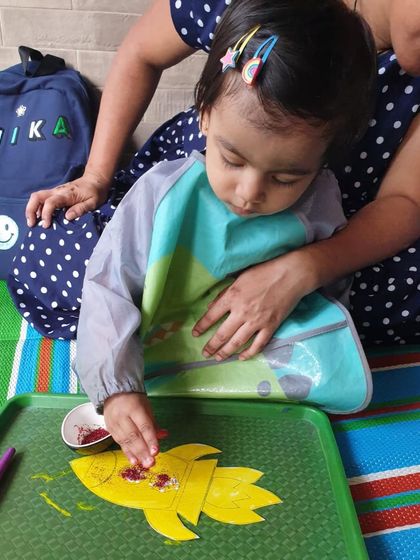 Adding some sparkle to a paper rocket. This little astronaut is using glitter to make her creation shine, adding a fun sensory element to our space craft session.