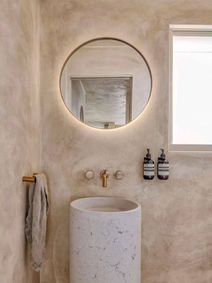 Venetian plaster is a trending material that we love to use. This bathroom showcases its beautiful, subtle texture on the walls, creating a soft, polished look around the cylindrical sink and backlit mirror.